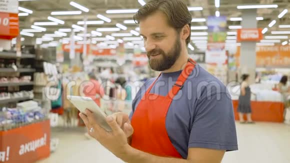 超级市场帅哥店员在超市里用触摸屏平板电脑他正对着摄像机微笑视频的预览图