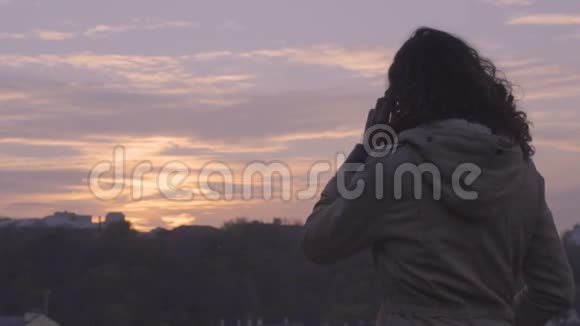 混合种族的女人在智能手机上对着美丽的日落天空说话视频的预览图