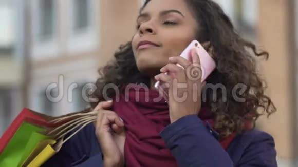 快乐的混血女人在智能手机上聊天拿着五颜六色的购物袋视频的预览图