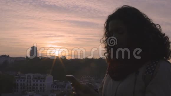 日落时分年轻快乐的女人在智能手机上发短信的剪影视频的预览图