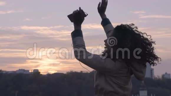 日落时分年轻自由的快乐女子在城市风景的背景下翩翩起舞视频的预览图