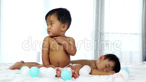两个婴儿在床上一个在玩彩球一个在睡觉视频的预览图