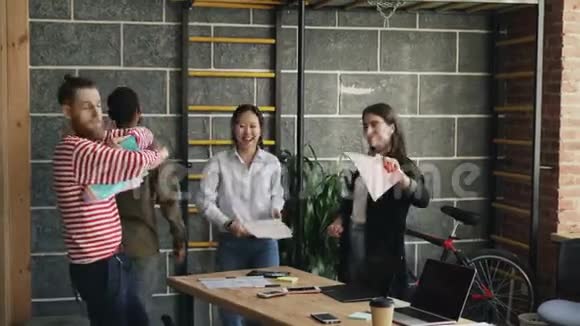 多民族创业的同事在现代办公室里跳舞扔纸文件庆祝视频的预览图