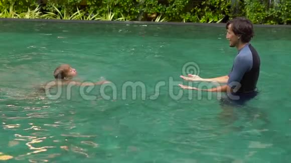 一位男子游泳教练在游泳池里教小男孩游泳的慢镜头视频的预览图