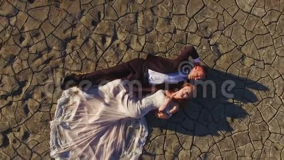 新娘和新郎躺在纹理地面上干盐湖视频的预览图