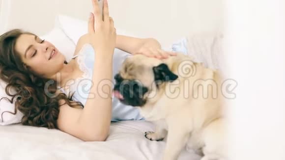 移动手机社交媒体在床上使用女人带着有趣的狗录像片段家庭阳光周末视频的预览图