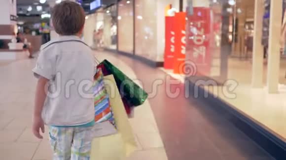 在时装店购物后一个拿着袋子的小男孩穿过商场视频的预览图