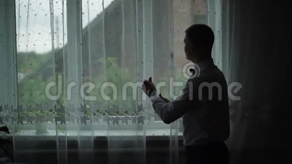 年轻人从家里的窗户欣赏风景穿上衬衫慢动作视频的预览图