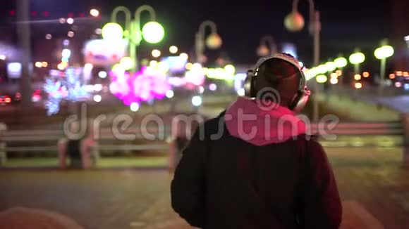 晚上在城市的大街上散步时戴着头戴电话的年轻人的肖像开始倾听视频的预览图