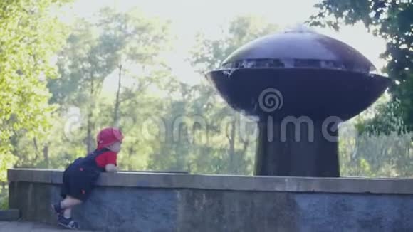 宝贝饶有兴趣地看着水站在喷泉附近的夏天公园的阴影4k慢速mo镜头视频的预览图