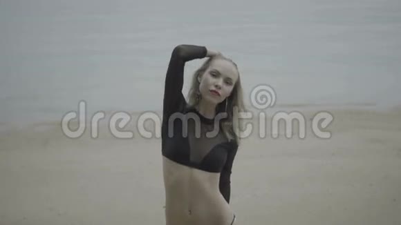 一位身穿黑色优雅泳衣的金发女子在海滩上的正面景色背景是慢动作视频视频的预览图