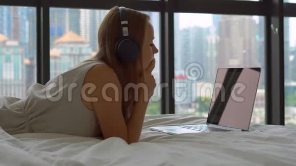 躺在床上的年轻女子用无线耳机听笔记本电脑上的音乐视频的预览图
