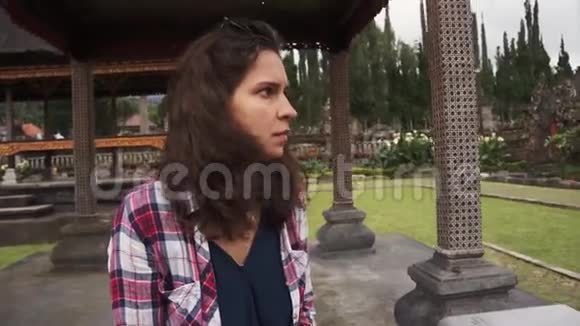 夏日巴厘岛公园的凉亭里坐着一位迷人的卷发女孩视频的预览图