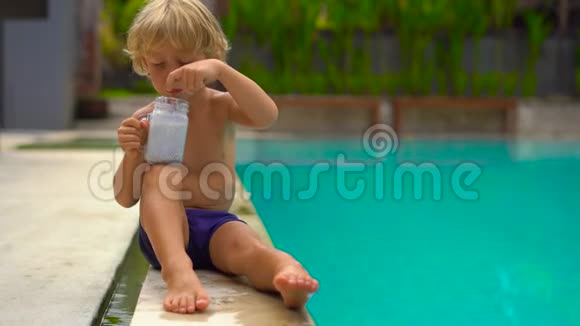 慢镜头的小男孩吃了一个辣椒布丁坐在一个游泳池的一侧视频的预览图