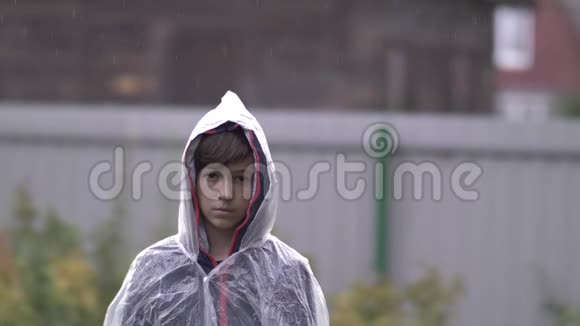 悲伤沮丧的男孩站在雨中的雨衣里慢动作视频的预览图