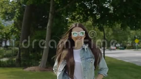 年轻女子戴着太阳镜和一件未系扣子的牛仔夹克在住宅区散步视频的预览图