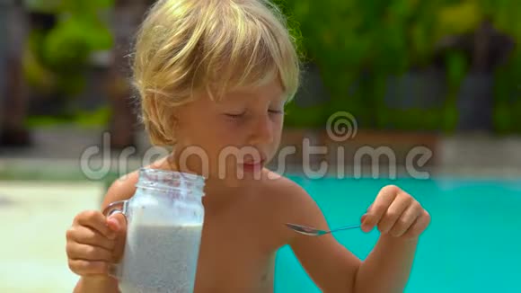慢镜头的小男孩吃了一个辣椒布丁坐在一个游泳池的一侧视频的预览图