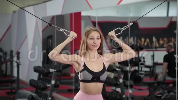 漂亮的运动年轻女孩在健身房的块模拟器上训练二头肌视频的预览图