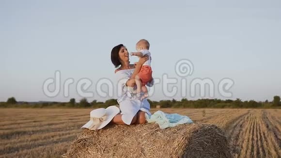 年轻女子和她的孩子在田里玩草包那个女孩正坐在田里的干草堆上玩得很开心视频的预览图