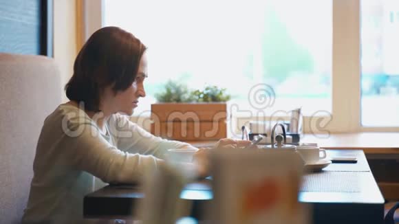 女人在咖啡馆喝茶手里拿着智能手机一位女士查看她的智能手机上的电子邮件并在视频的预览图