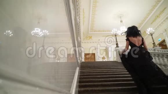年轻的黑发女子穿着黑色晚礼服在或酒店的大理石石梯上楼视频的预览图
