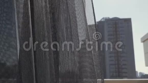 清晨窗上透明的灰色窗帘被风轻轻地抚摸着从窗户看到的城市景色视频的预览图