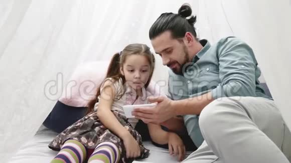 父亲带着快乐的小女儿玩智能手机用手机在Skype上聊天视频的预览图