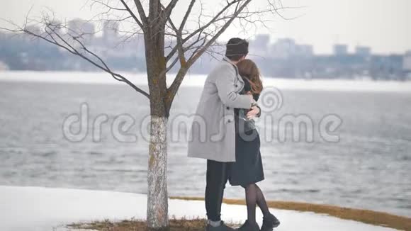 年轻的时髦男人和女人拥抱在河边的树下视频的预览图