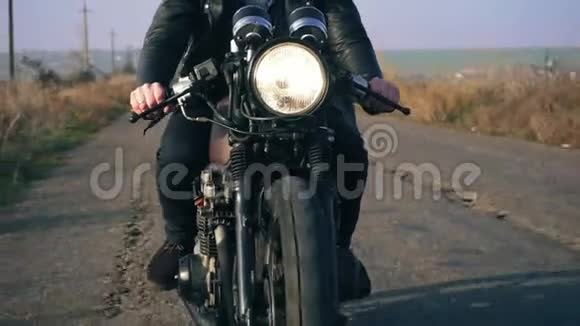 一位身穿黑色皮夹克骑摩托车手持车把的人在乡间小路上的前景大人物视频的预览图