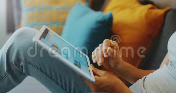 高质量的4k12位镜头美丽的女孩使用平板电脑坐在家里的沙发上女人上网社交视频的预览图