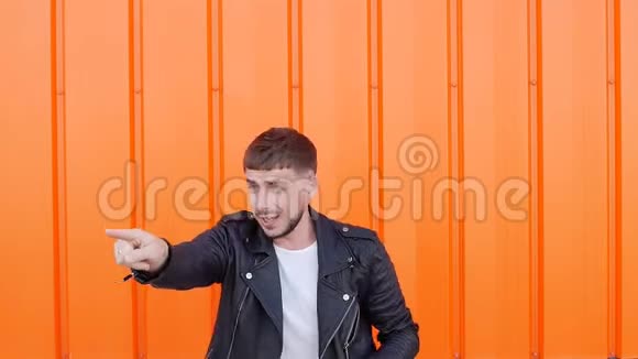 白人年轻积极情绪化的男性黑发穿着黑色夹克在橙色背景下跳舞特写视频的预览图