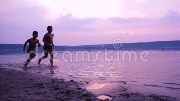 两个男孩沿着河岸奔跑的剪影视频的预览图
