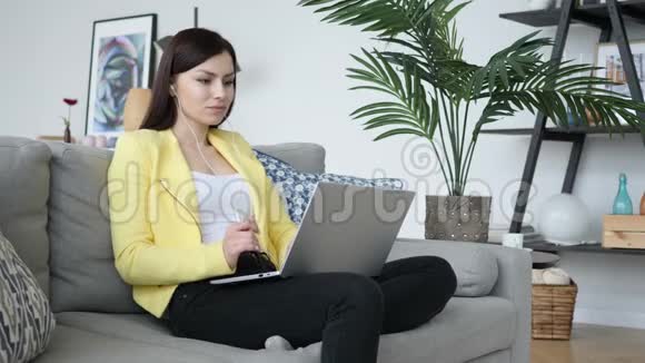 休闲坐着的女人在家的笔记本电脑上听音乐视频的预览图