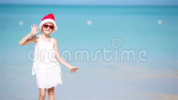 戴圣诞帽的小可爱女孩在白色沙滩上过圣诞假期视频的预览图