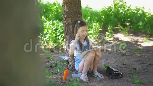 夏天白种人的小女孩坐在树下用画笔画画视频的预览图