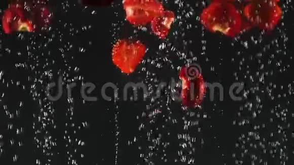 落下来的新鲜红色草莓片溅到闪闪发光的水在黑色的背景关门视频的预览图