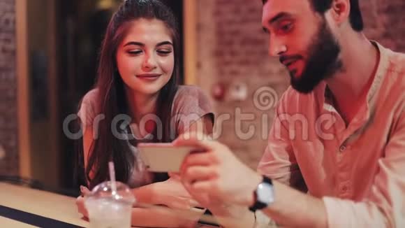 快乐的年轻夫妇有智能手机聊天和饮料坐在酒吧使用手机智能手机的朋友视频的预览图