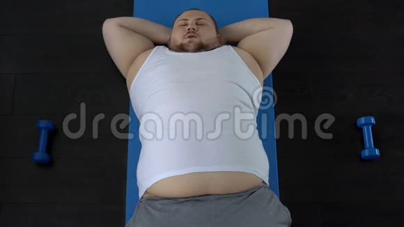 懒惰的超重男人做仰卧起坐和在地板上休息遗传倾向视频的预览图