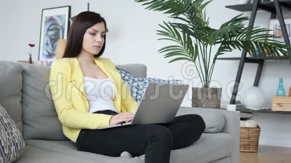 生病的创意女人一边咳嗽一边用沙发和打字在笔记本电脑上视频的预览图