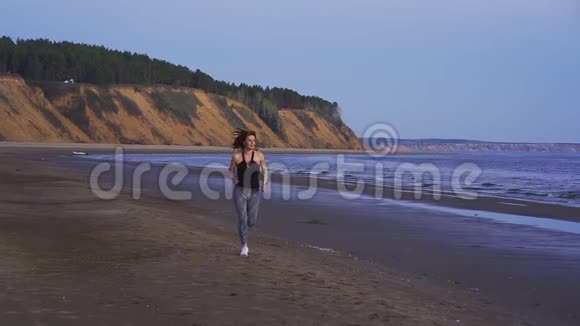 慢动作身材苗条的中年妇女穿着运动制服红头发在一个夏天的早晨沿着沙岸奔跑视频的预览图