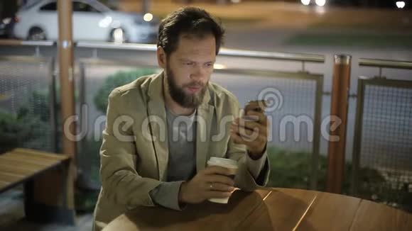白种人中年商人晚上下班后坐在一家夏天的咖啡馆里手里拿着一部电话视频的预览图