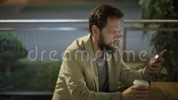 白种人中年商人晚上下班后坐在一家夏天的咖啡馆里手里拿着一部电话视频的预览图