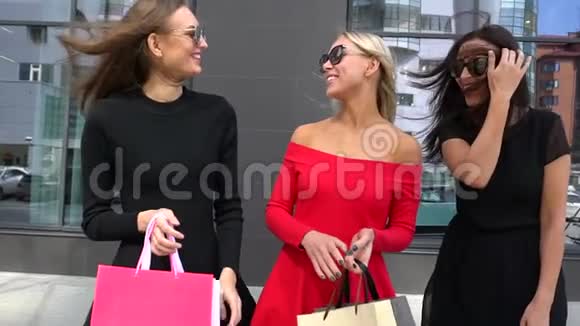年轻的女朋友们在购物的快乐日子里大笑购物女孩展示购买的东西三个快乐的女人购物后视频的预览图