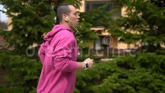 运动员运动男子跑步在绿色公园树林训练和看智能手表拉丁嘻哈跑者视频的预览图