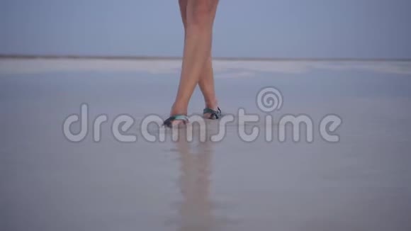 日落时分穿着绿色凉鞋的女孩在盐湖的水洼中飞溅视频的预览图