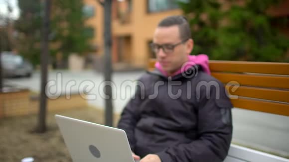 快乐的人在笔记本电脑上工作20多岁快乐的学生在笔记本电脑上浏览互联网坐在户外年轻的潮人视频的预览图