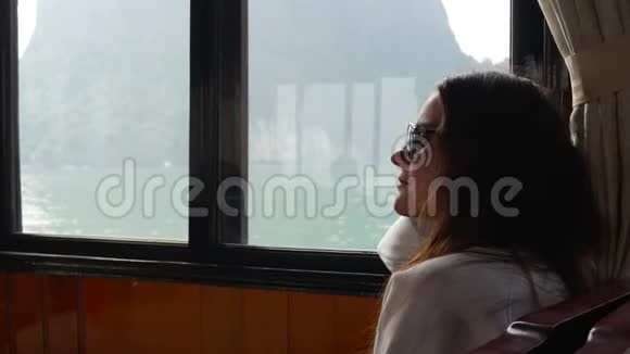 一位年轻女子穿着白色毛衣和太阳镜坐在船里正注视着海湾的美丽景色视频的预览图