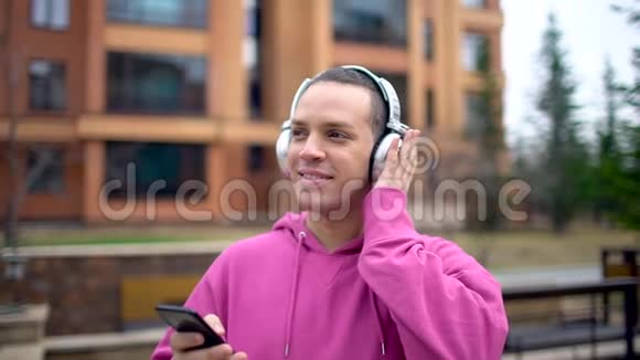 年轻人在街上用耳机一个有智能手机的人在城市街道旁散步年轻的白种人视频的预览图