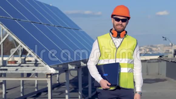 一名工人对着照相机微笑同时站在太阳能电池板附近拿着一台笔记本电脑4K视频的预览图