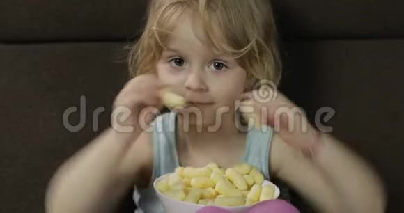 女孩坐在沙发上吃玉米泡芙儿童微笑品尝爆米花视频的预览图